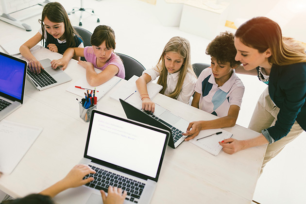 Niños combinan tablets y cuadernos en clase, guiados por su maestra. Foto: MultiBriefs