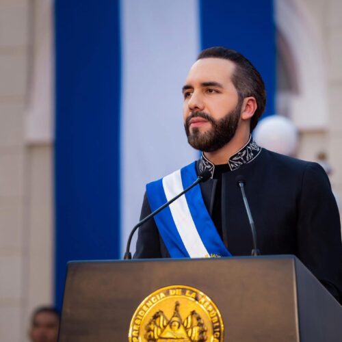 Nayib Bukele durante un discurso, con la bandera salvadoreña de fondo, simbolizando su postura soberanista. Su rechazo al "wokismo" y políticas de género divide opiniones entre admiradores y críticos internacionales. (Foto: archivo X @nayibbukele)