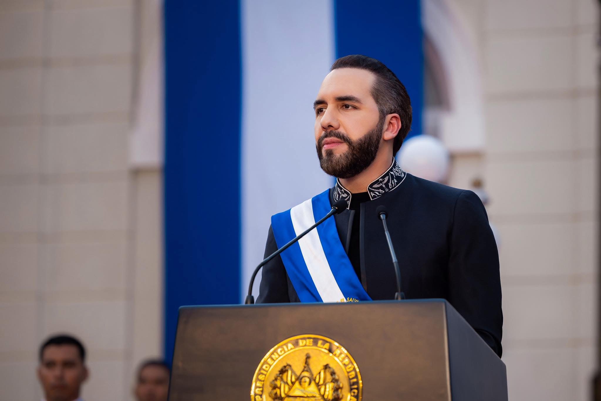 Nayib Bukele durante un discurso, con la bandera salvadoreña de fondo, simbolizando su postura soberanista. Su rechazo al "wokismo" y políticas de género divide opiniones entre admiradores y críticos internacionales. (Foto: archivo X @nayibbukele)
